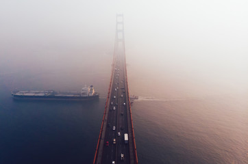 Aerial view of Golden Gate Bridge in foggy visibility during evening time, metropolitan transportation  infrastructure, birds eye view of automotive car vehicles on road of suspension construction
