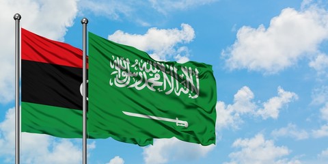 Libya and Saudi Arabia flag waving in the wind against white cloudy blue sky together. Diplomacy...