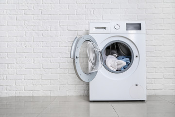 Modern washing machine with laundry near white brick wall