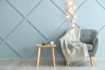 Armchair with table near grey wall with glowing garland