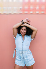 Portrait of happy pretty curly brunette woman laughing by pink wall