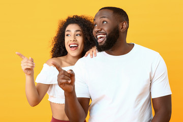 Portrait of happy African-American couple pointing at something on color background