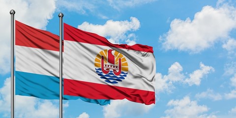 Luxembourg and French Polynesia flag waving in the wind against white cloudy blue sky together. Diplomacy concept, international relations.