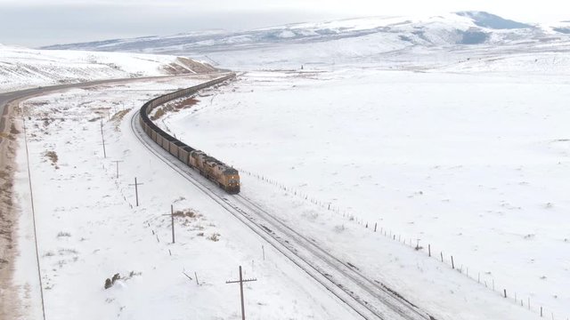 AERIAL: Flying along a locomotive transporting coal across the snowy United States. Cinematic shot of a freight train transporting cargo from a coal mine to a storage depot on other side of America.