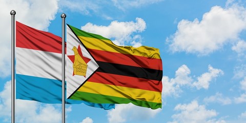 Luxembourg and Zimbabwe flag waving in the wind against white cloudy blue sky together. Diplomacy concept, international relations.