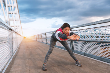 Fitness woman stretching on the bridge at sunset