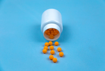 Yellow pills and plastic white bottle. Blue background with copy space for text.