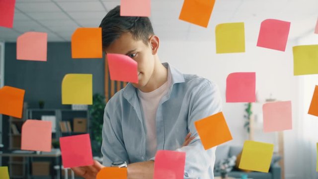 Creative businessman brainstorming ideas working with sticky notes on glass in office. Worker man in modern office.