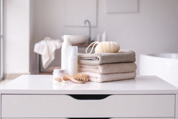 Fototapeta na wymiar Stack of towels, cosmetics, loofah and brushes on table in bathroom
