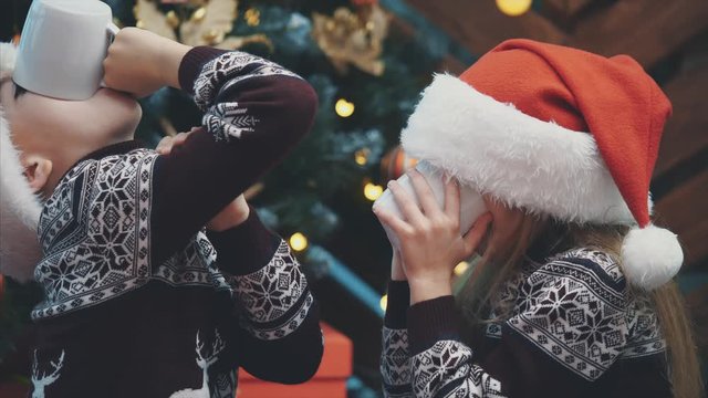 Happy twins drinking cocoa on Christmas eve and then giving thumbs up, showing that it was really tasty.