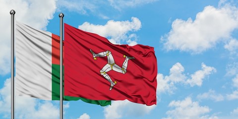 Madagascar and Isle Of Man flag waving in the wind against white cloudy blue sky together....