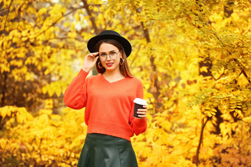 Stylish young woman with cup of coffee in autumn park