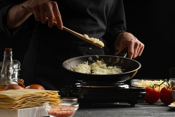 Chef fries onions in a pan, against the background of ingredients. Home recipe book, delicious food, gastronomy
