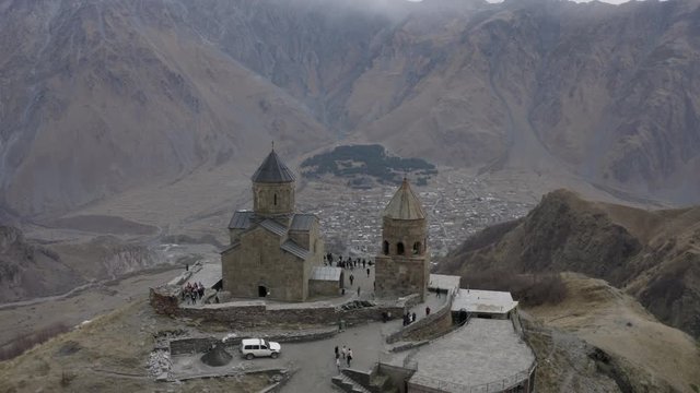 Aerial flying around view ancient georgian church on highland on Kazbek mountain. Old orthodox temple Gergeti Georgia, Stepantsminda on city and mountain valley background