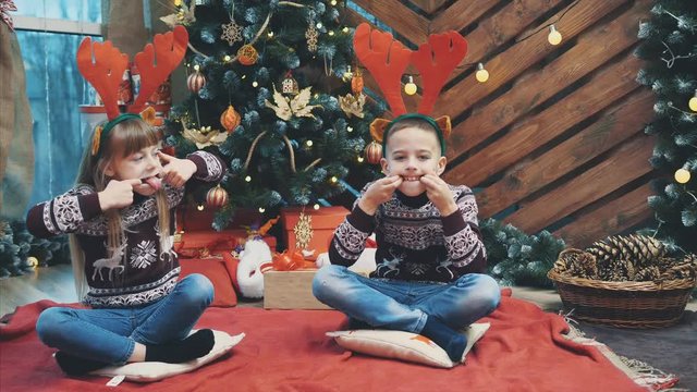 4k video of funny children putting on reindeer antlers headgear, making grimaces on new year evening.