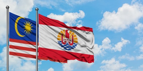 Malaysia and French Polynesia flag waving in the wind against white cloudy blue sky together. Diplomacy concept, international relations.