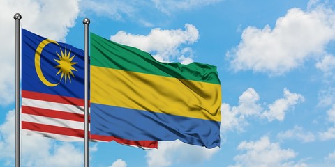 Malaysia and Gabon flag waving in the wind against white cloudy blue sky together. Diplomacy...