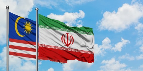 Malaysia and Iran flag waving in the wind against white cloudy blue sky together. Diplomacy...