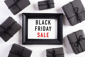 Top view of Black Friday Sale text on white picture frame with black gift box and Christmas ball and berries on white background. Shopping concept and black Friday composition.