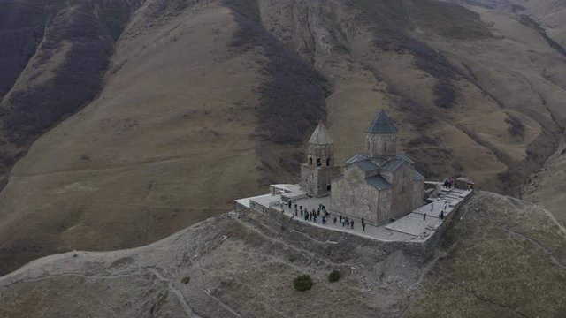 Aerial around view ancient georgian church on highland on Kazbegi mountain. Old orthodox temple Gergeti Georgia, Stepantsminda on city and mountain valley background