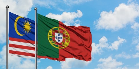 Malaysia and Portugal flag waving in the wind against white cloudy blue sky together. Diplomacy concept, international relations.