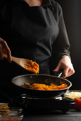 cooking, lasagna, cook prepares dressing, frying in a pan. Black background. Italian-European cuisine. Vertical shot.