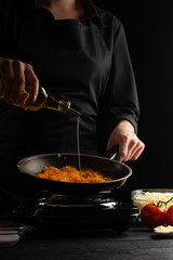 cooking, lasagna, cook prepares dressing, frying in a pan pouring olive oil. Black background. Italian-European cuisine. Vertical frame