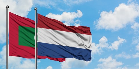 Maldives and Netherlands flag waving in the wind against white cloudy blue sky together. Diplomacy...
