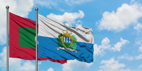 Maldives and San Marino flag waving in the wind against white cloudy blue sky together. Diplomacy...