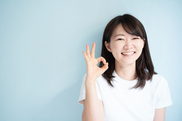 Young woman shoing OK gesture against light blue background