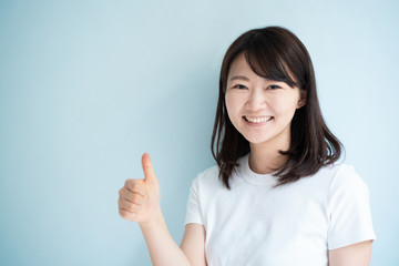 Young woman showing thumb up gesture against light blue background