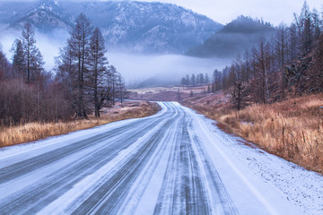 A picturesque mountain road stretching into the distance to the mountains covered with dense fog.