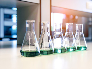 The Erlenmeyer or Conical flasks on bench laboratory, with range of green solvent forming reaction between boric acid and ammonia solution analysis concentration in wastewater sample. Selective focus.