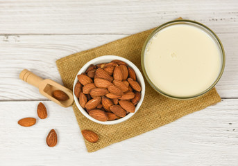 Almond milk in bowl and almonds on wooden scoop on sack