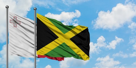 Malta and Jamaica flag waving in the wind against white cloudy blue sky together. Diplomacy concept, international relations.