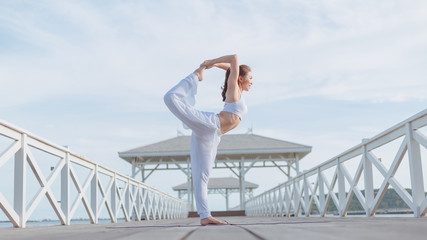 Young women practice yoga on the white bridge by the sea, the concept of enjoying privacy and the...