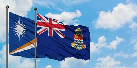 Marshall Islands and Cayman Islands flag waving in the wind against white cloudy blue sky together....