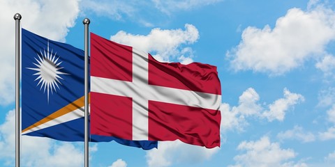 Marshall Islands and Denmark flag waving in the wind against white cloudy blue sky together....