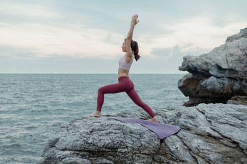 Young woman doing yoga exercise yoga master pose on the rock. Amazing yoga landscape in beautiful...
