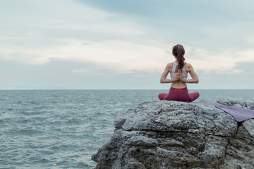 Young women doing yoga, exercising outdoors on the rocks The beautiful landscape, the sunrise of...
