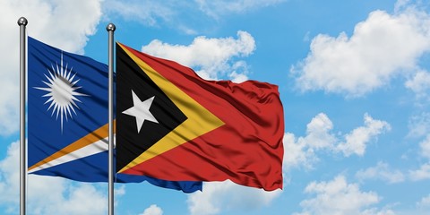 Marshall Islands and East Timor flag waving in the wind against white cloudy blue sky together. Diplomacy concept, international relations.