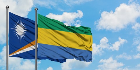 Marshall Islands and Gabon flag waving in the wind against white cloudy blue sky together....