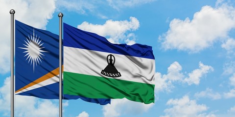 Marshall Islands and Lesotho flag waving in the wind against white cloudy blue sky together....
