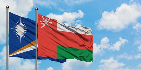 Marshall Islands and Oman flag waving in the wind against white cloudy blue sky together. Diplomacy concept, international relations.