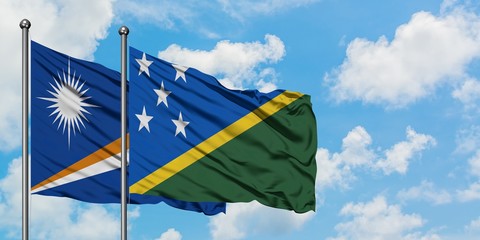 Marshall Islands and Solomon Islands flag waving in the wind against white cloudy blue sky together. Diplomacy concept, international relations.