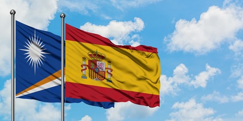 Marshall Islands and Spain flag waving in the wind against white cloudy blue sky together. Diplomacy concept, international relations.