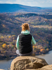 Teenage girl sits on the cliff of Breakneck Ridge trail - obrazy, fototapety, plakaty
