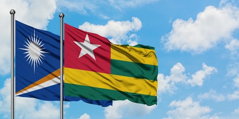 Marshall Islands and Togo flag waving in the wind against white cloudy blue sky together. Diplomacy...