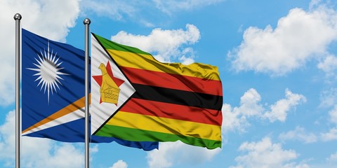 Marshall Islands and Zimbabwe flag waving in the wind against white cloudy blue sky together. Diplomacy concept, international relations.