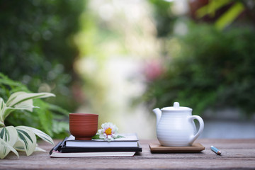 White teapot and vintage cup with flower and notebooks on wooden table